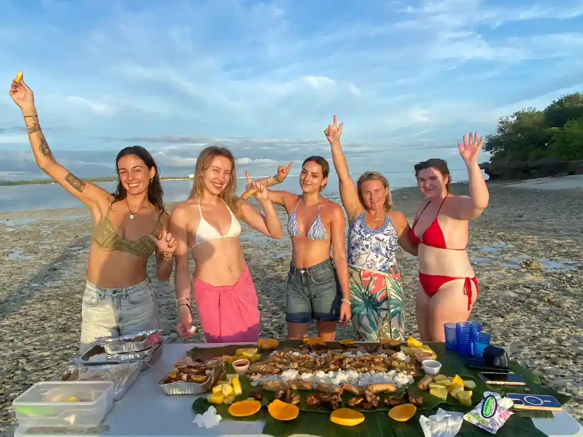 Travellers around a Filipino boodle fight laid out on banana leaves on a sandbar at sunset, Bohol