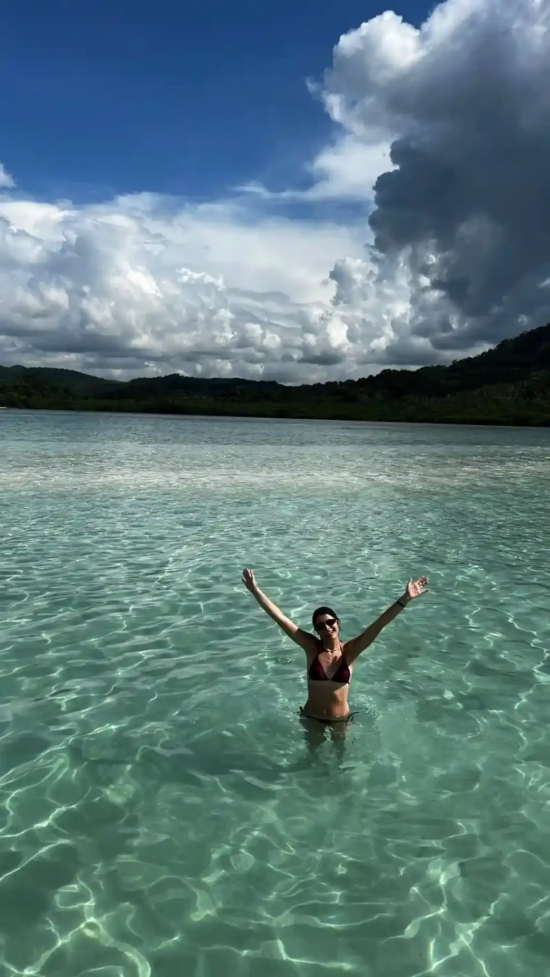 Traveller standing in clear shallow water as cloud builds over the headland, Philippines