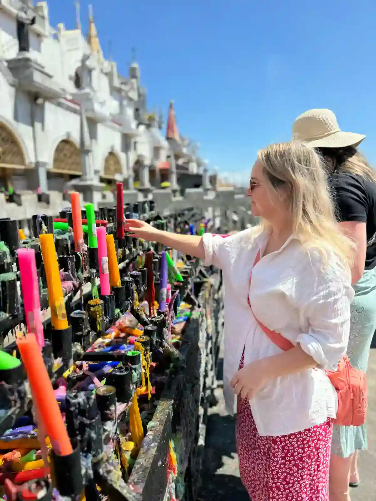 Traveller lighting a candle among rows of coloured candles at Simala Shrine, Cebu